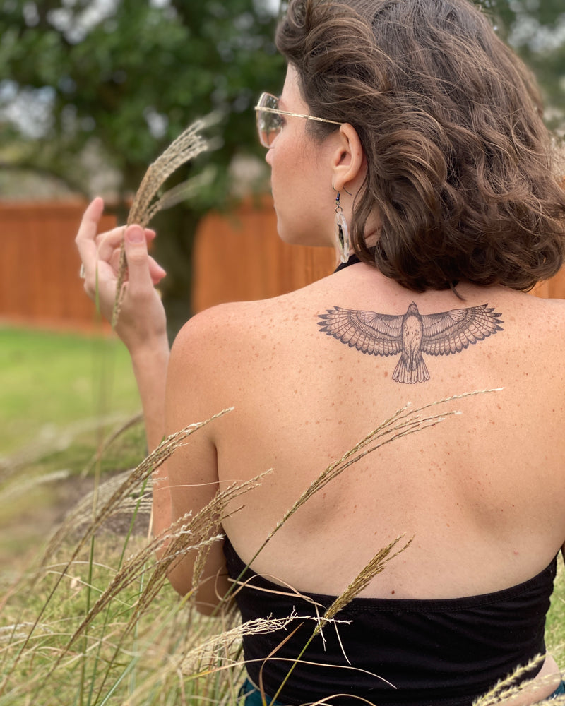 hawk temporary tattoo on persons back wearing black with a nature green background 