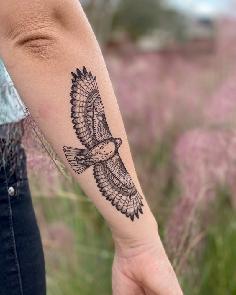 hawk temporary tattoo on the back of a persons arm wearing blue jeans in a blurred floral nature background 