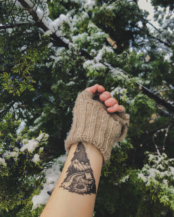mountain camping temporary tattoo on persons wrist wearing brown in a green nature background 