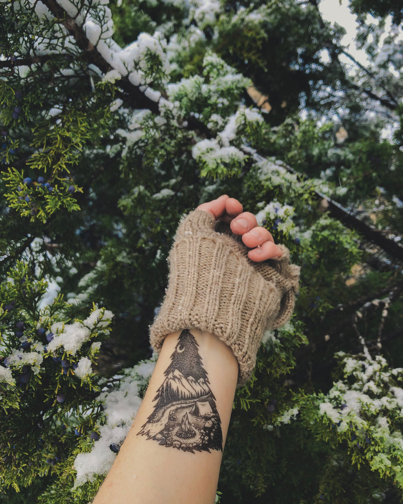 mountain camping temporary tattoo on persons wrist wearing brown in a green nature background 