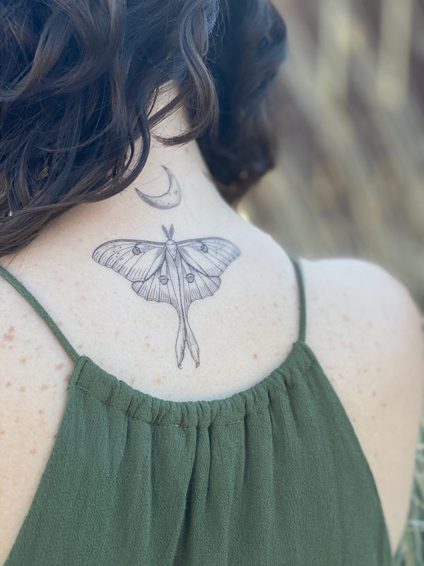 Temporary tattoo of a Luna moth on a person's neck, displayed in black lines with a crescent moon above it.