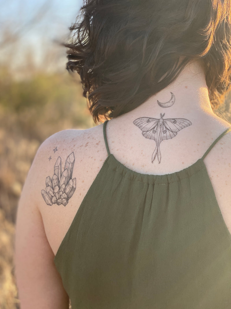Luna Moth with crescent moon above it temporary tattoo on persons neck wearing green in a blurred nature background 