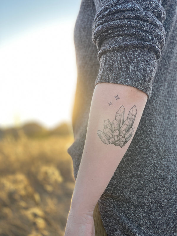 quartz crystal temporary tattoo on persons arm wearing grey in a blurred nature background 