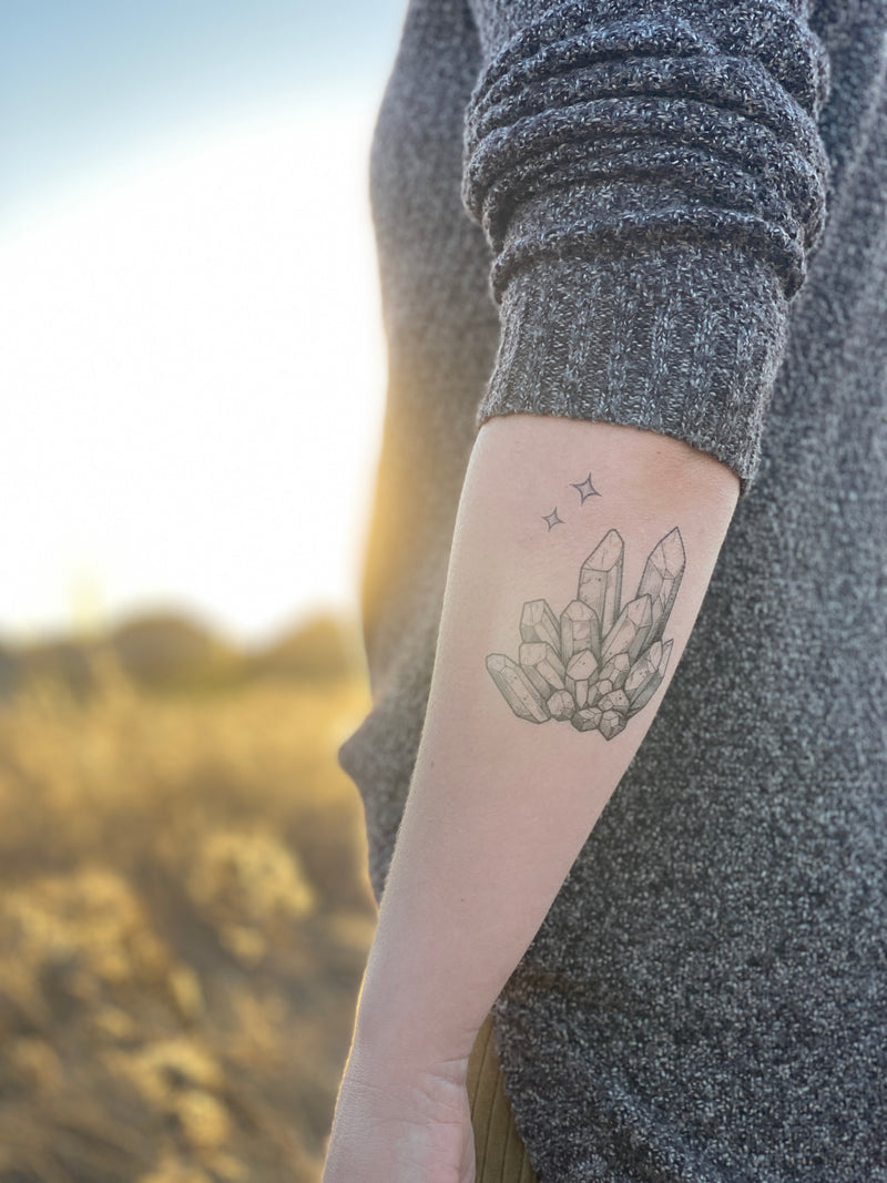 quartz crystal temporary tattoo on persons arm wearing grey in a blurred nature background 
