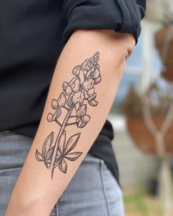 A person's forearm featuring a temporary tattoo of a bluebonnet flower with surrounding leaves.