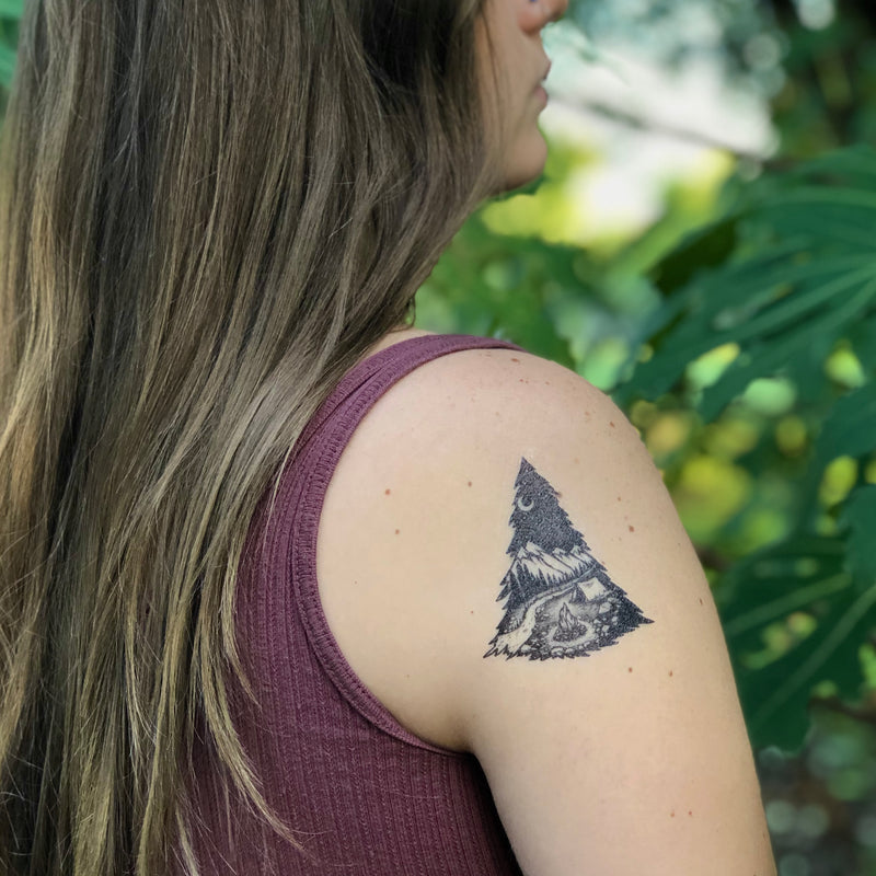 mountain camping temporary tattoo on persons shoulder wearing dark red in a green nature background 