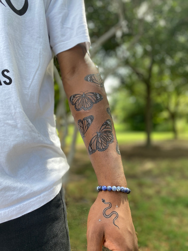 Monarch Butterfly temporary tattoos on persons arm wearing white and black in a blurred green nature background 