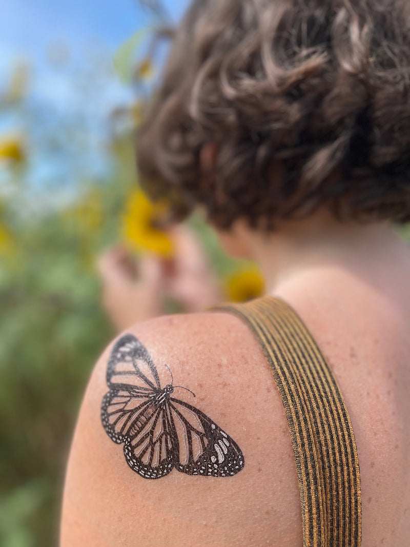 Monarch butterfly temporary tattoo on person shoulder wearing yellow in a blurred nature background 