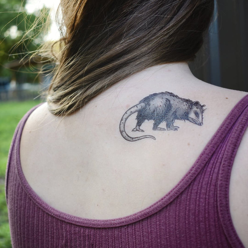 opossum temporary tattoo on persons back wearing dark red with brown hair in a nature background 