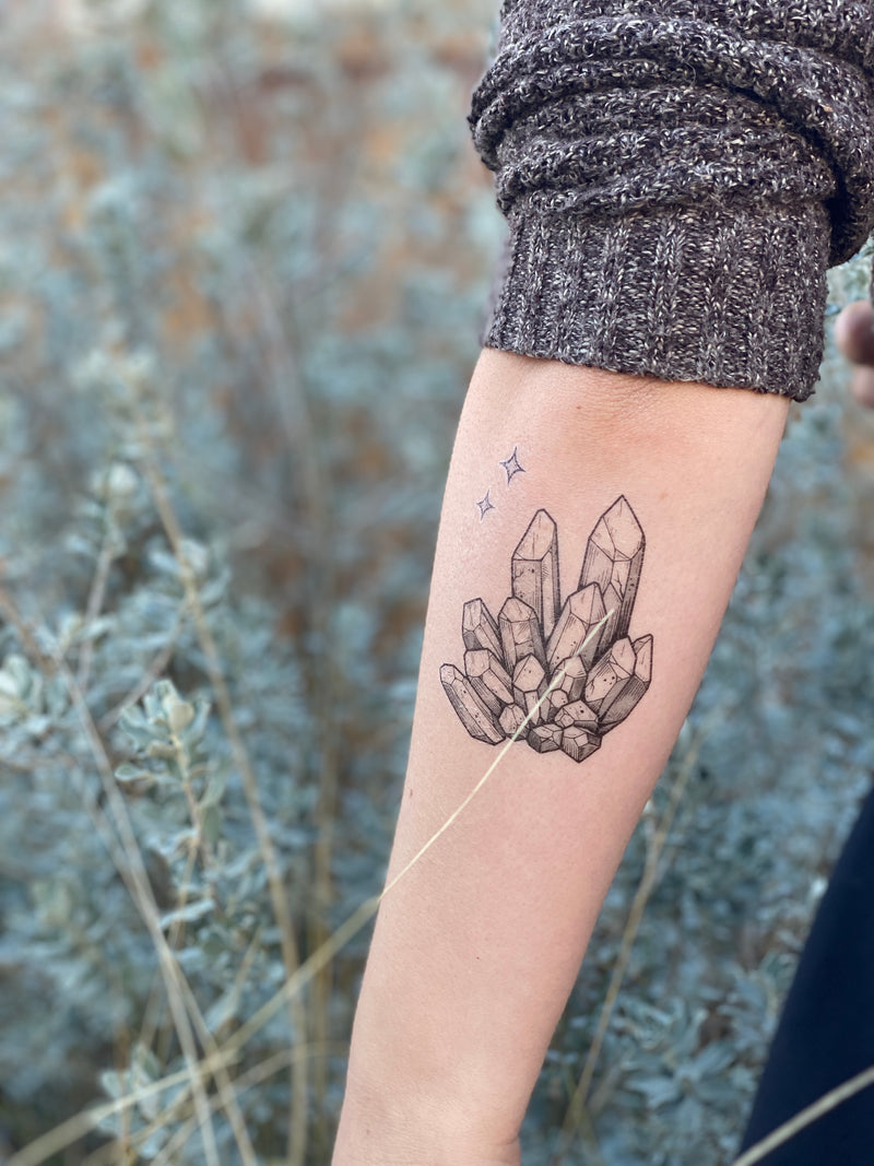 quartz crystal temporary tattoo on persons arm wearing grey in a blurred nature background 