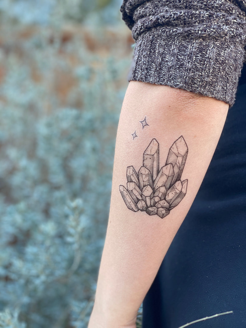 A temporary tattoo of a quartz crystal design, applied on the forearm, showcasing black line art against the skin.