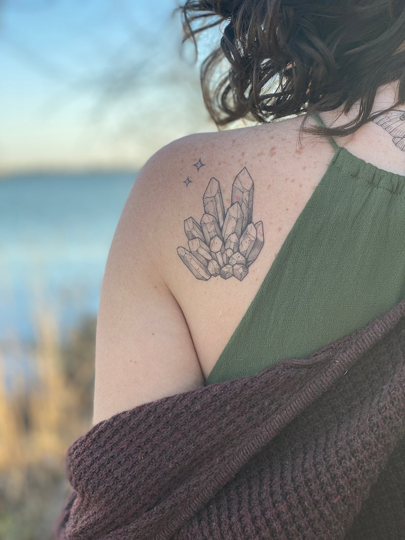 quartz crystal temporary tattoo on persons back wearing green and dark red in a blurred nature background 