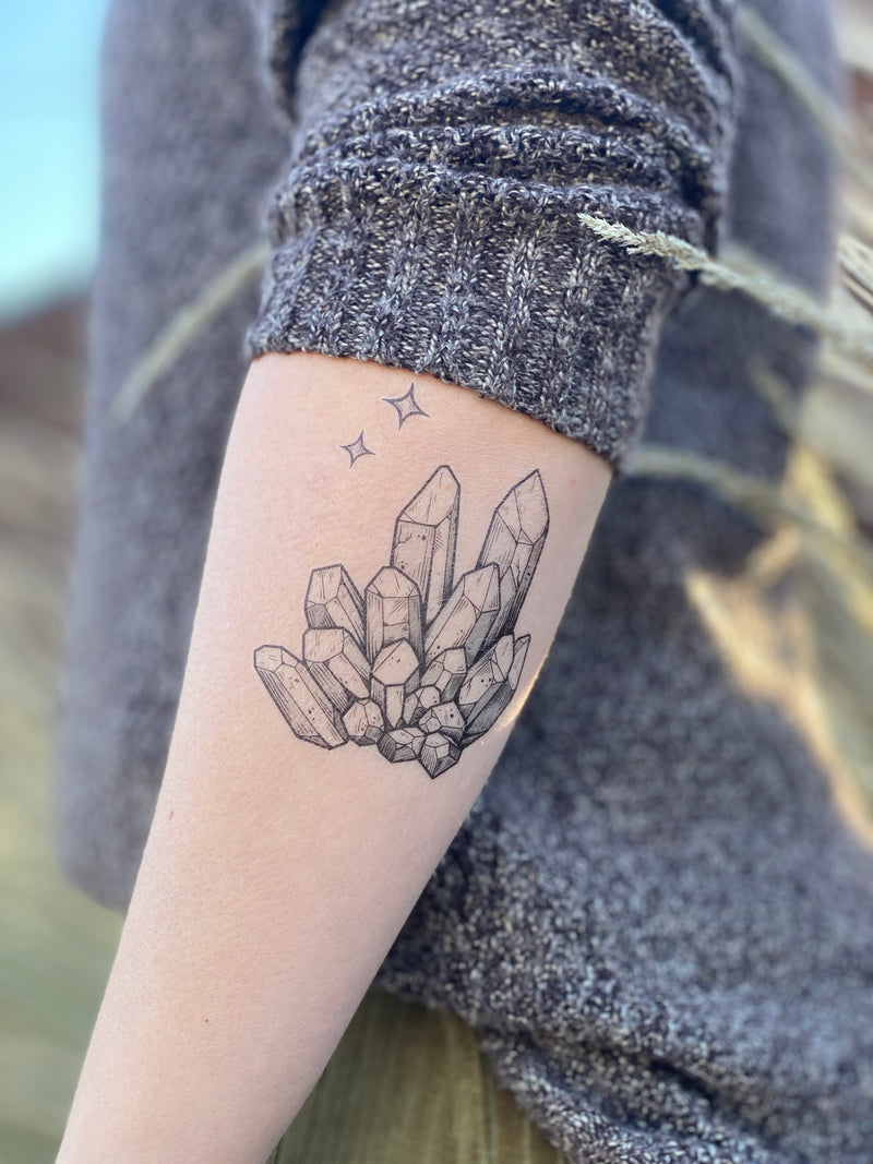 quartz crystal temporary tattoo on persons arm wearing grey in blurred nature background 