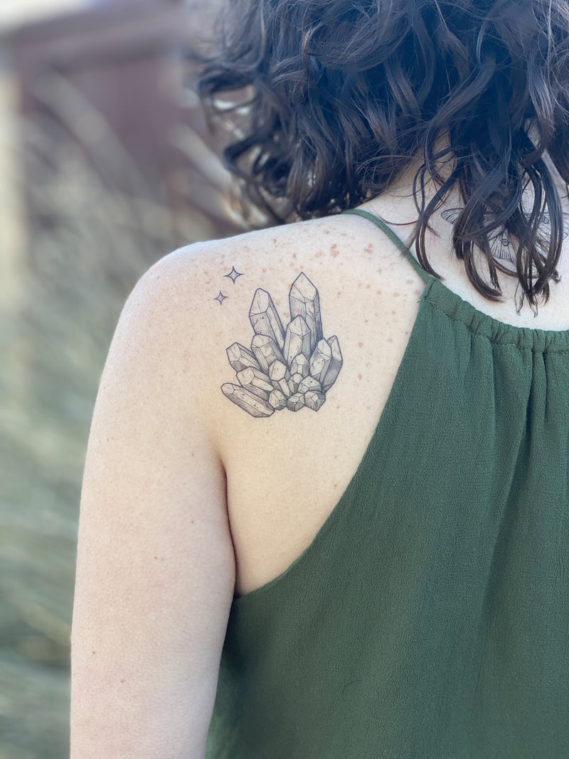 quartz crystal temporary tattoo on persons back wearing green in a blurred nature background 